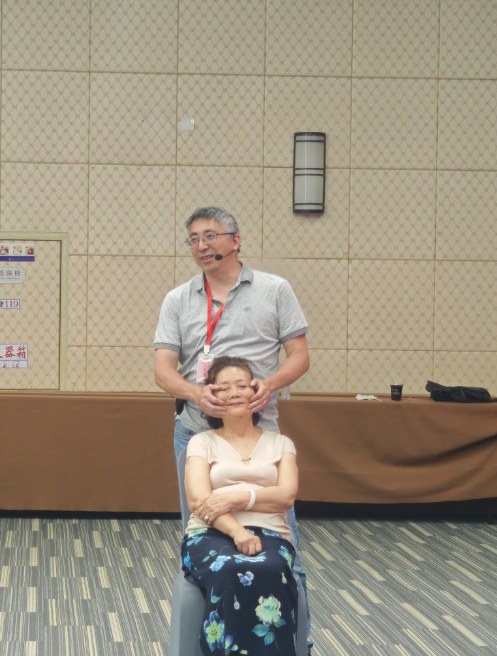 Dr. Yu standing behind a seated student, demonstrating a headache Tui-Na technique