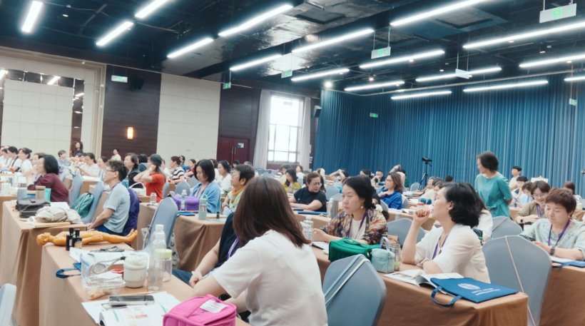 Attendees seated at long tables in the lecture hall, listening to a session